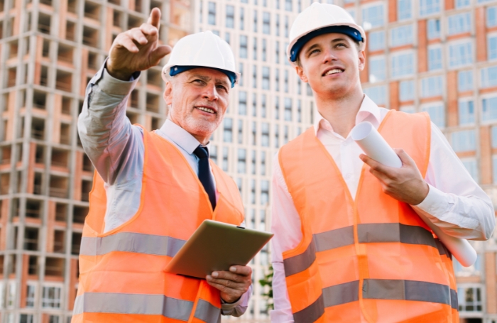 Two male architects on site dressed in hiviz jackets and hard hats discussing a projectjpg