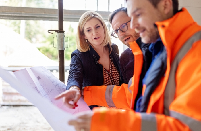 A group of three architects on a building site looking at and discussing a diagramjpg A group of three architects on a building site looking at and discussing a diagram